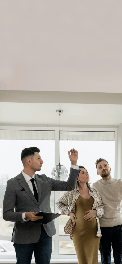 Um corretor apresentando um imóvel para um homem e uma mulher em pé em uma sala.