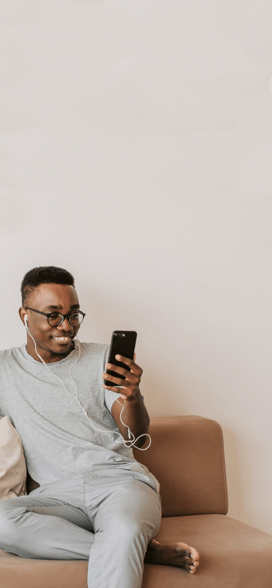 Um homem sentado em um sofá segurando um telefone celular com um sorriso no rosto.