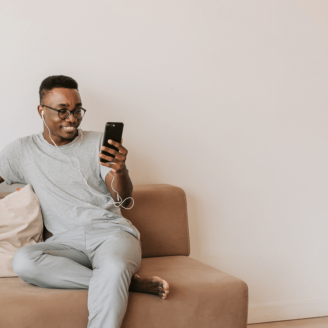 Um homem sentado em um sofá segurando um telefone celular com um sorriso no rosto.