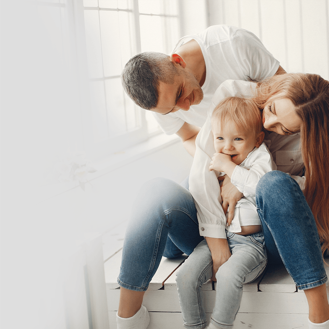 Um homem, uma mulher e uma criança estão sentados em um banco, todos estão sorrindo.