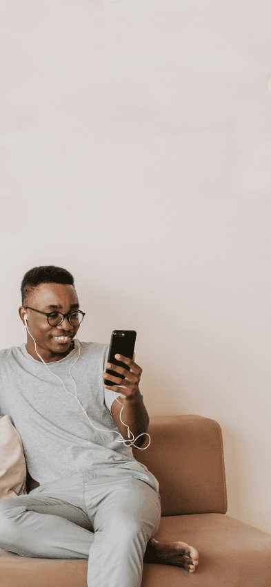 Um homem sentado em um sofá segurando um telefone celular com um sorriso no rosto.