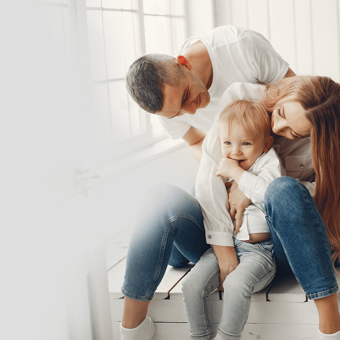 Um homem, uma mulher e uma criança estão sentados em um banco, todos estão sorrindo.