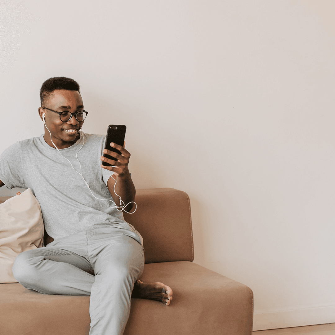 Um homem sentado em um sofá segurando um telefone celular com um sorriso no rosto.