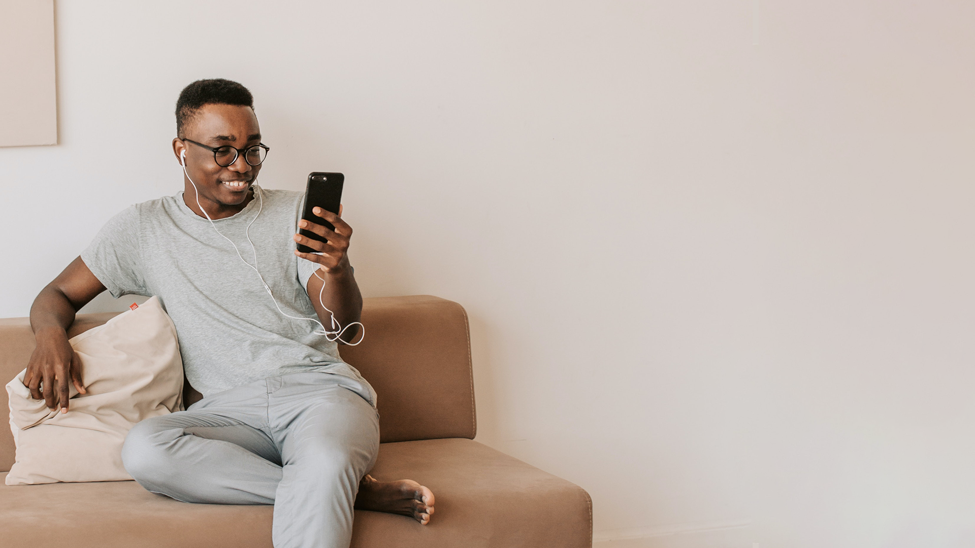 Um homem sentado em um sofá segurando um telefone celular com um sorriso no rosto.